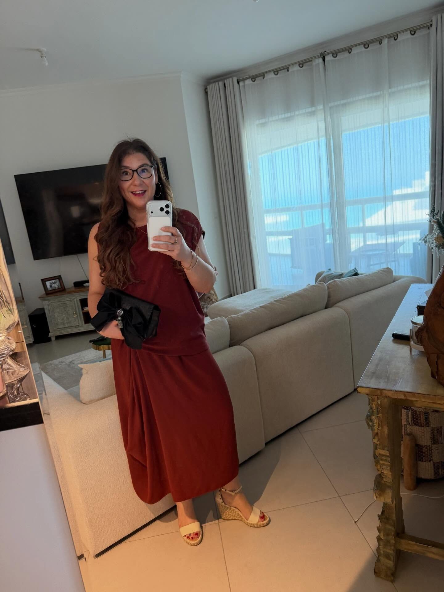Vanessa in a long red dress, taking a mirror selfie in a bright living room